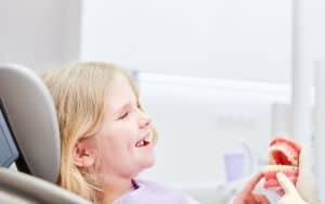 Fröhliches Mädchen als Patient sitzt angstfrei beim Zahnarzt